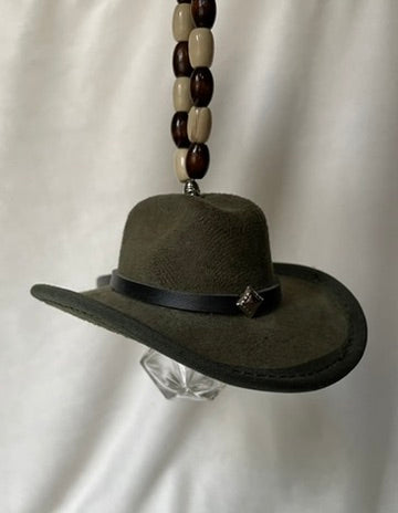 Olive green miniature cowboy hat with a black band hanging from a beaded elastic loop on a white background