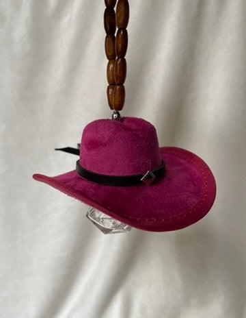 Pink miniature cowboy hat with a black band hanging from a beaded elastic loop on a white background