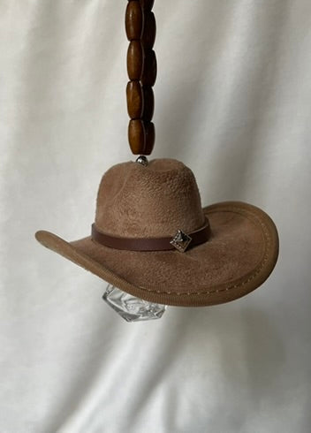Tan miniature cowboy hat with a brown hat band hanging from a beaded elastic loop on a white background